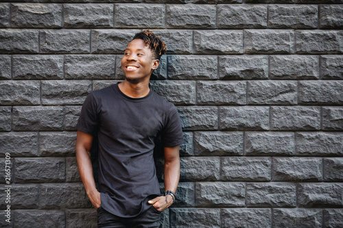 Handsome african american man in blank black t-shirt standing against brick wall