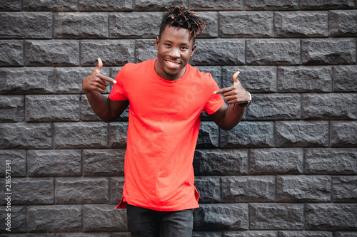 Mockup, african man model showing empty red t-shirt against brick wall
