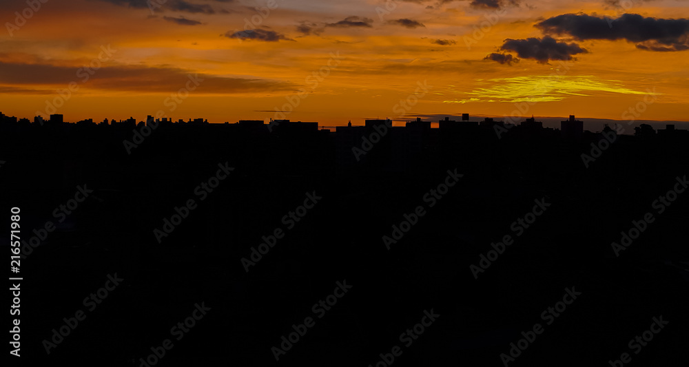 A frontal view of a beautiful and striking sunset in the northern part of Porto Alegre, showing the silhouette of the buildings, with reddish and yellowish tones and a few city lights