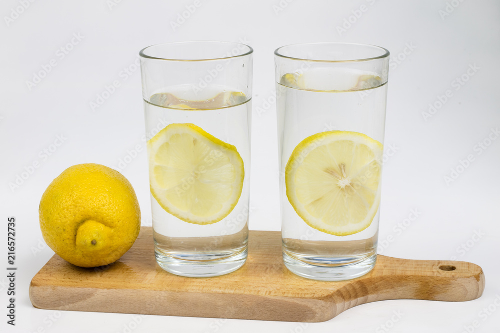 Fototapeta premium A glass of cold water with lemon on a white kitchen table. A refreshing drink in warm weather.