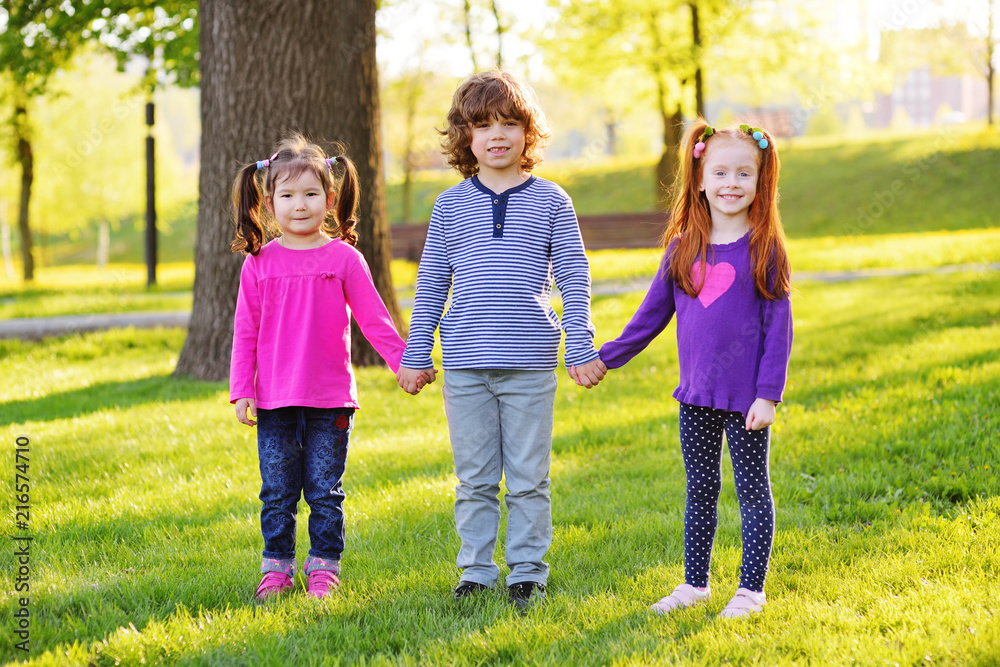 a group of small children smiling holding hands on a background of grass, a tree and a park. Children's Day, June 1, friendship, childhood.