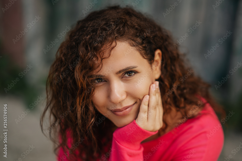 Obraz premium Close up portrait of a cheerful curly young woman smiling outdoors