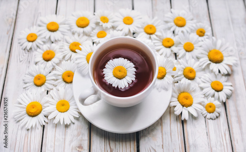 Cup of chamomile tea with fresh daisies. White fresh flowers on a light gray vintage wooden background. The concept of a sedative.