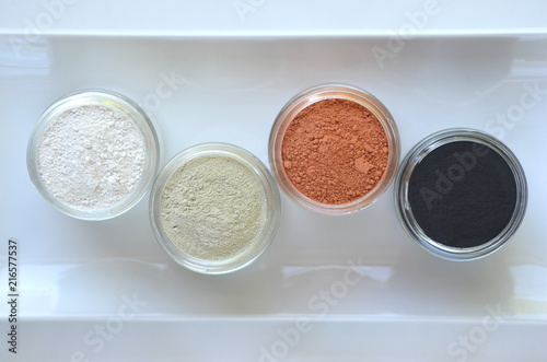 Top view of kaolin powder, activated charcoal, red, green and green cosmetic clays in jars. Deep cleansing bentonite (montmorillonite) clay for beauty spa face mask, body detox and hair treatments. 