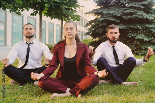 Three friends in business clothes barefoot doing yoga on the grass