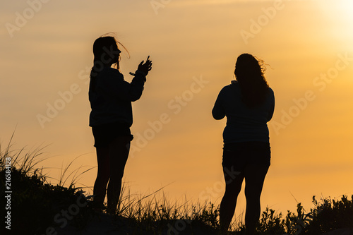 Two women silhouetted  by the setting sun on a sand dune in Assateague Island. photo