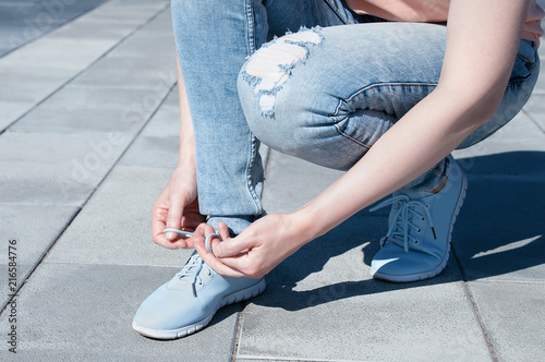 The girl is tying shoelaces on sneakers. Close-up.