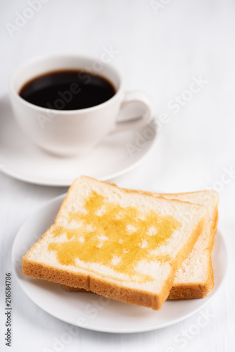 Sliced bread with honey topping and cup of black coffee on white table, delicious breakfast