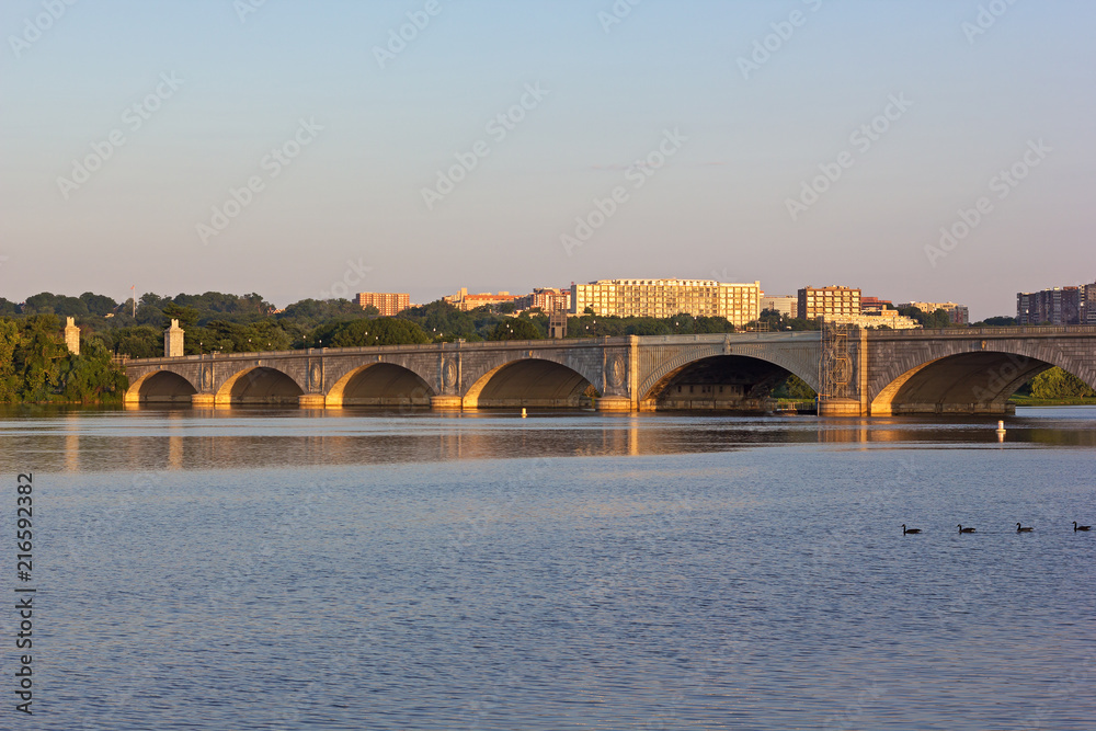 Obraz premium Arlington Memorial Bridge and Rosslyn suburb at sunrise, Washington DC, USA. Panoramic view on Potomac River and Washington DC metro area buildings across the river.