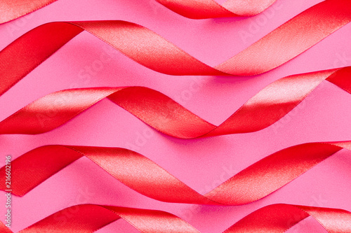 Curled red satin ribbons on pink background, horizontal