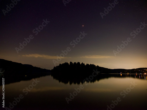 夜の湖畔にて、島の真上に火星と星座、湖面はオレンジ色で鏡の様に映っす。