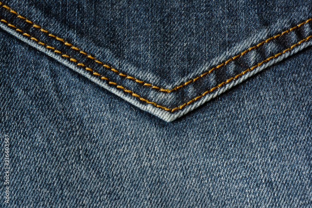 Close-up of a piece of blue jeans with orange stitches. Pocket close-up. Close-up of a piece of blue jeans with orange stitches. Pocket close-up.