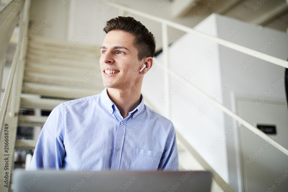 Fototapeta premium Young contemporary businessman in earphones sitting on staircase and enjoying music during work