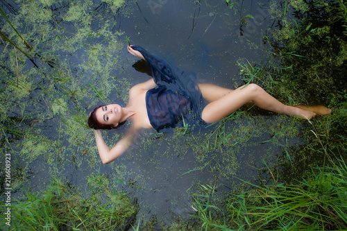 a young woman lies in a swamp covered with a black cloth