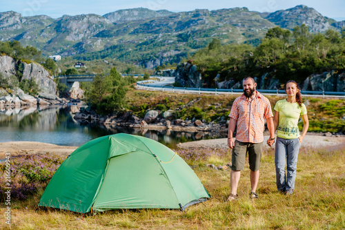 Sportive couple hiking resting near the tent in the warm sunshine at morning. Travel, vacation, holidays and adventure concept. Lake, Road, Mountain landscape background