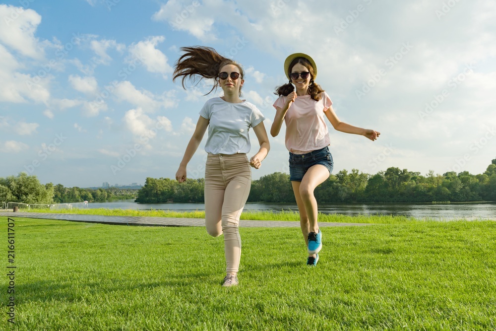 Young girls are running. Teenagers having fun on the green lawn in the park, enjoying sunny summer day. Young girls are running. Teenagers having fun on the green lawn in the park, enjoying sunny summer day.