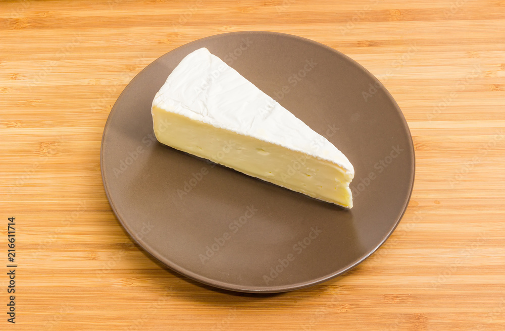 Piece of brie cheese on brown dish on wooden surface