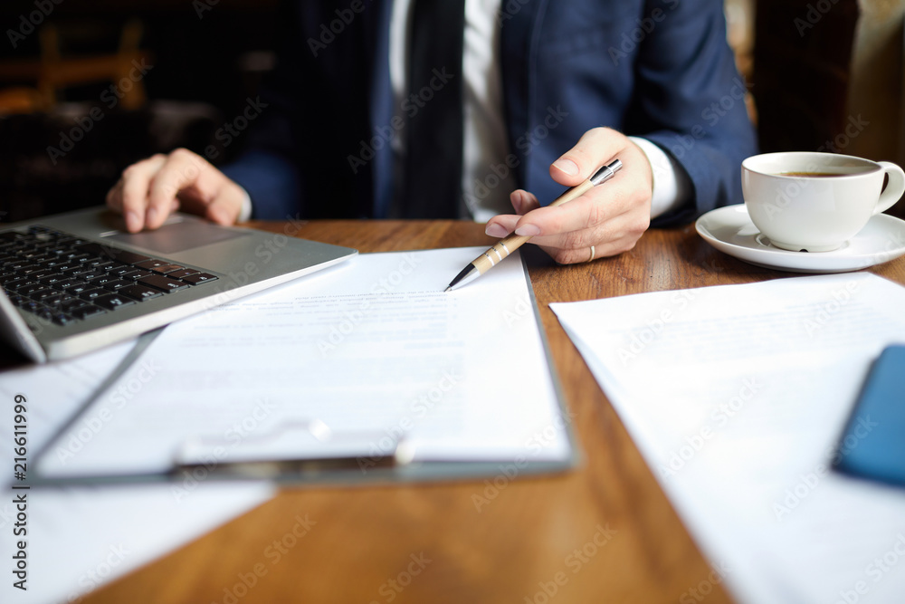 Close-up of unrecognizable businessman reading contract content and pointing with pen at text while correcting file using laptop Close-up of unrecognizable businessman reading contract content and pointing with pen at text while correcting file using laptop