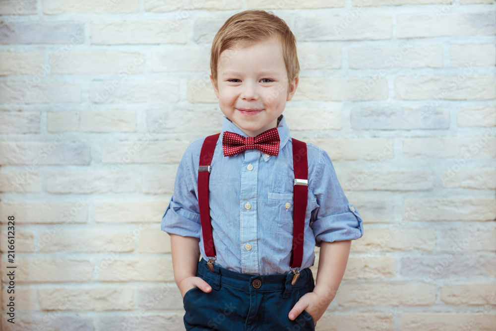 Smiling child boy in fashionable clothes on brick wall background Smiling child boy in fashionable clothes on brick wall background