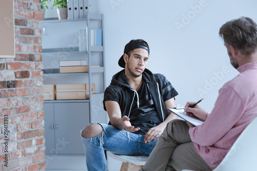 A rebel teenage boy with behavioral problems and criminal past talking to a psychotherapist in a juvenile detention center. photo