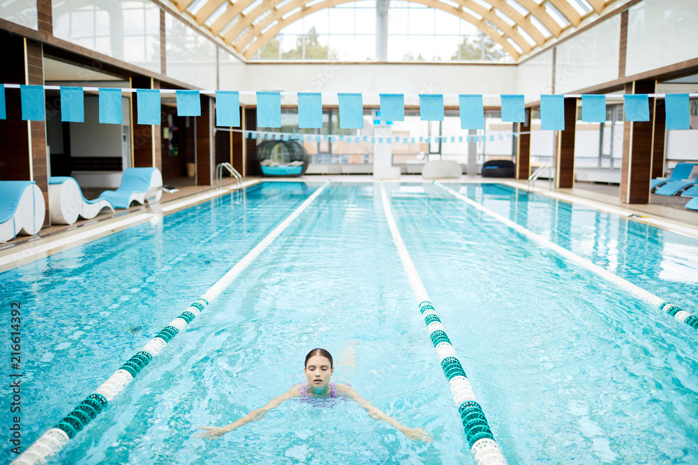 Obraz premium Sporty girl swimming along one of tracks in pool of luxurious spa resort