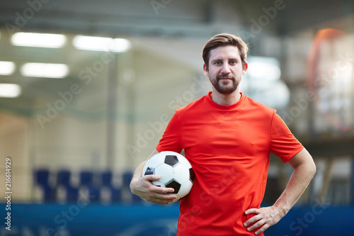 Young football player in red uniform holding soccer ball with the other hand on his waist © pressmaster