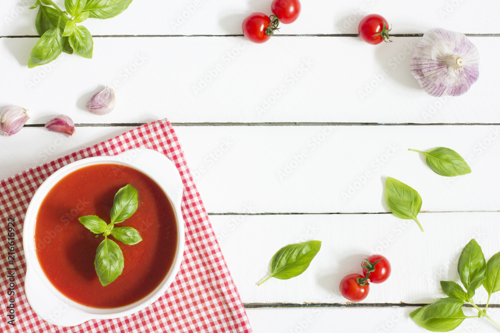 
Creamy tomato soup with basil and garlic on white wooden kitchen table 