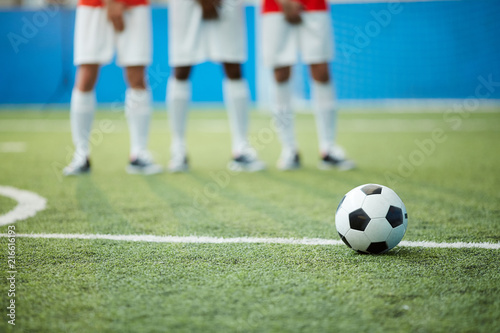 Fototapeta Naklejka Na Ścianę i Meble -  Soccer ball on green football field by dividing line and legs of three players on background