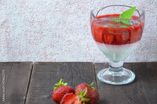 Summer dessert, panna cotta or yogurt or pudding or jam with strawberrieswith strawberries decorated with mint leaves. On a brown wooden table, bright sunlight. Copy space. close up photo