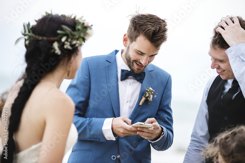 Groom occupied with phone at beach wedding ceremony photo