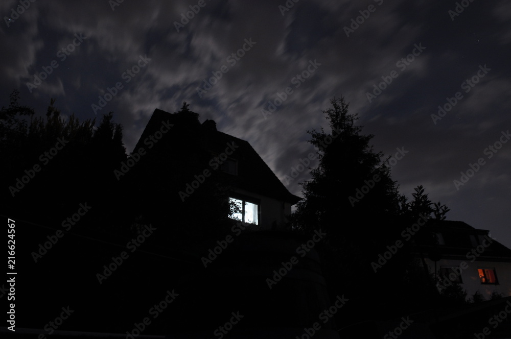 einzelnes erleuchtetes Fenster bei Nacht in einem von Bäumen umgebenen Haus einzelnes erleuchtetes Fenster bei Nacht in einem von Bäumen umgebenen Haus