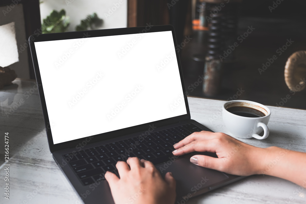 Mockup image of a woman using and typing on laptop with blank white screen and coffee cup on table in modern cafe Mockup image of a woman using and typing on laptop with blank white screen and coffee cup on table in modern cafe