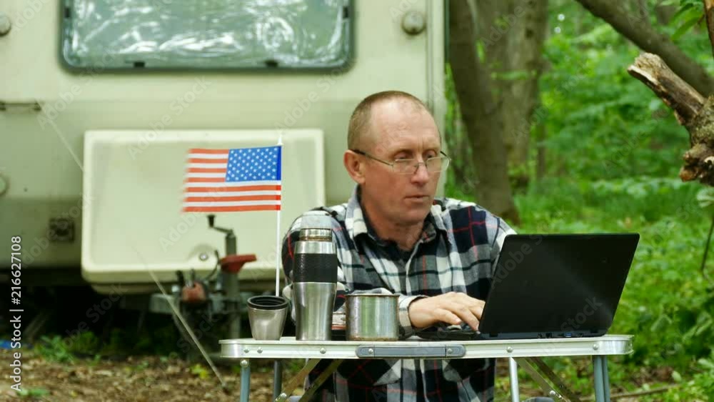 4K. American man traveler works on laptop near trailer camping and think . Freelance life 4K. American man traveler works on laptop near trailer camping and think . Freelance life