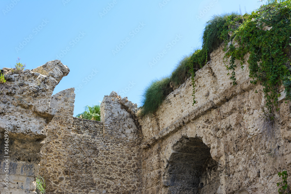 a stone wall of limestone with an arched niche overgrown with green loam. part of the ancient city. Side, Turkey