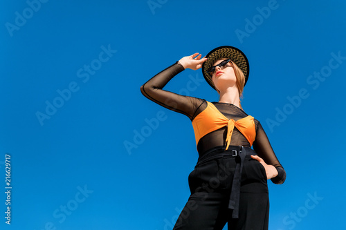 stylish girl posing in trendy sunglasses and hat, blue sky on background