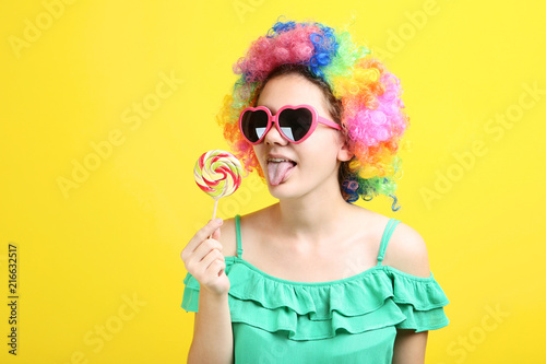Young girl in clown wig and lillopop on yellow background