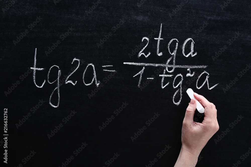 Female hand writing maths formulas on chalkboard Female hand writing maths formulas on chalkboard