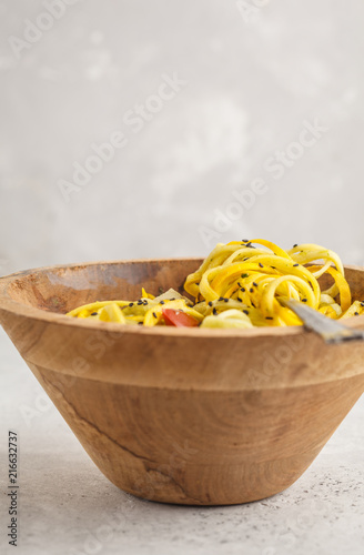 Raw vegan zucchini noodles with tofu and tomatoes in a wooden bowl.