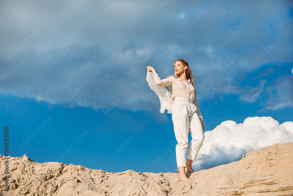 charming fashionable model in white trendy clothes with silk scarf walking on sand dune charming fashionable model in white trendy clothes with silk scarf walking on sand dune