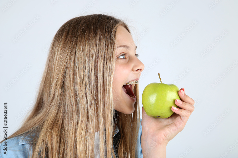 Young smiling girl with dental braces and green apple on grey background Young smiling girl with dental braces and green apple on grey background