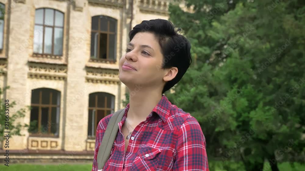 Happy young college student with black short hair smiling and standing in park near university Happy young college student with black short hair smiling and standing in park near university