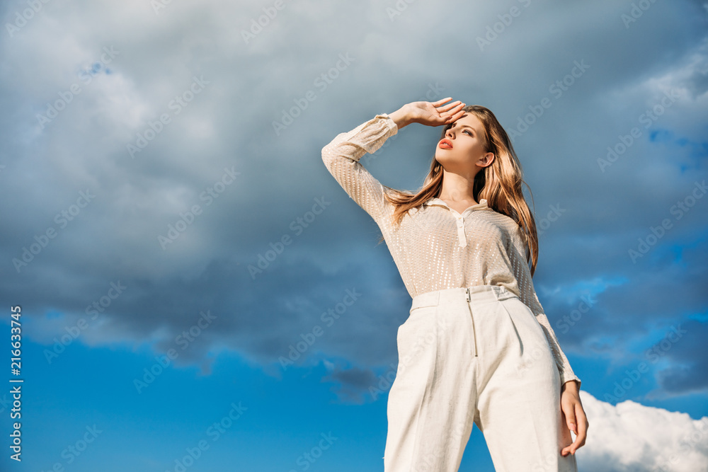 bottom view of elegant blonde woman posing in white clothes with cloudy sky on background bottom view of elegant blonde woman posing in white clothes with cloudy sky on background