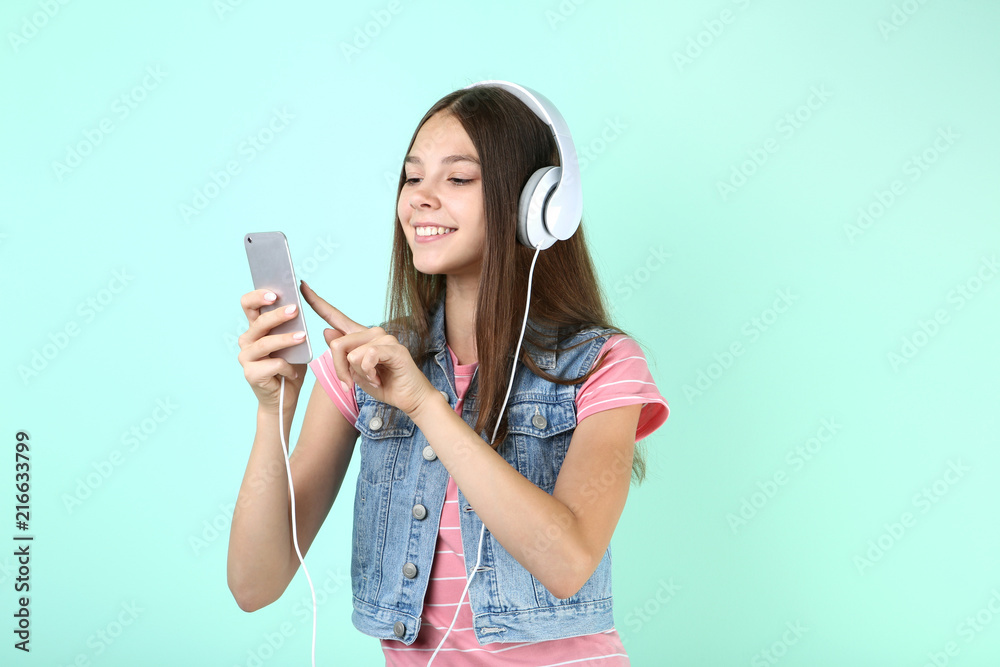 Young girl with headphones and smartphone on mint background