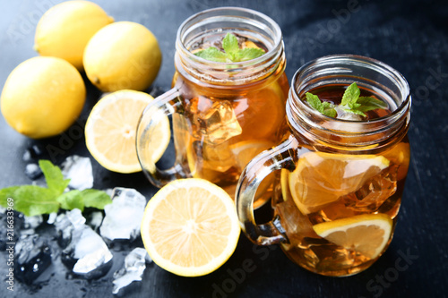 Ice tea in glass jars with lemon and mint leafs on wooden table