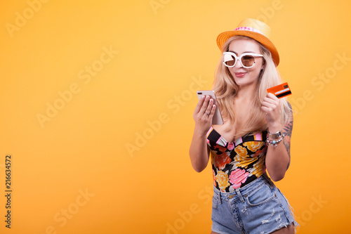 Beutiful woman holds smart phone and credit card in studio on yellow background