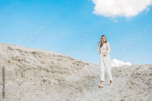 beautiful woman in white fashionable clothes posing on sand dune with blue sky
