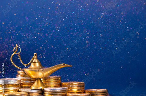 Magic lamp of wishes on stacks of gold coins with golden dust. Studio shooting. photo