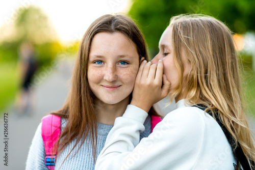 Two girl friends schoolgirl. In the summer in city. Tells a friend in the ear, a secret, really. The concept of surprise, best friends, gift. Emotion of happiness is the pleasure of a smile.