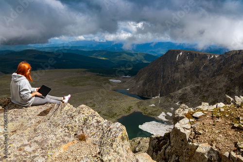 Young tourist man working on a laptop and sitting on the top of the mounting and looking at a beautiful landscape. Freelancer works outside the office. 