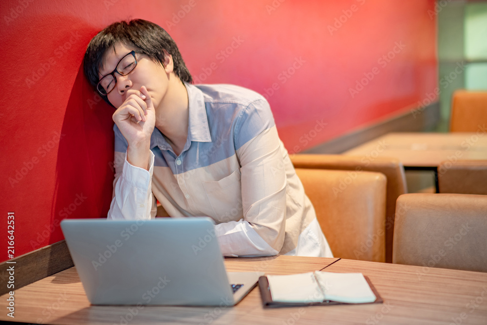 Young Asian businessman with eyeglasses feeling stressed, frustrated and tired while working with laptop computer in red cafe. Business problem concept. Young Asian businessman with eyeglasses feeling stressed, frustrated and tired while working with laptop computer in red cafe. Business problem concept.